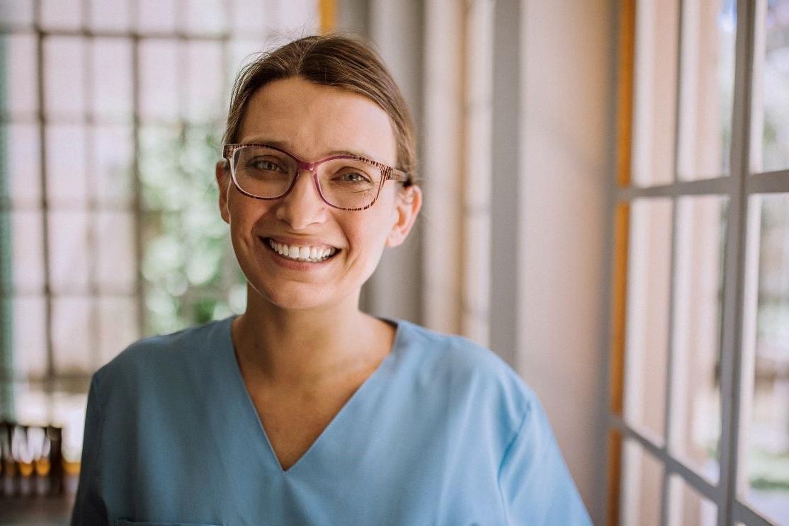 nurse smiling and standing next to a window 